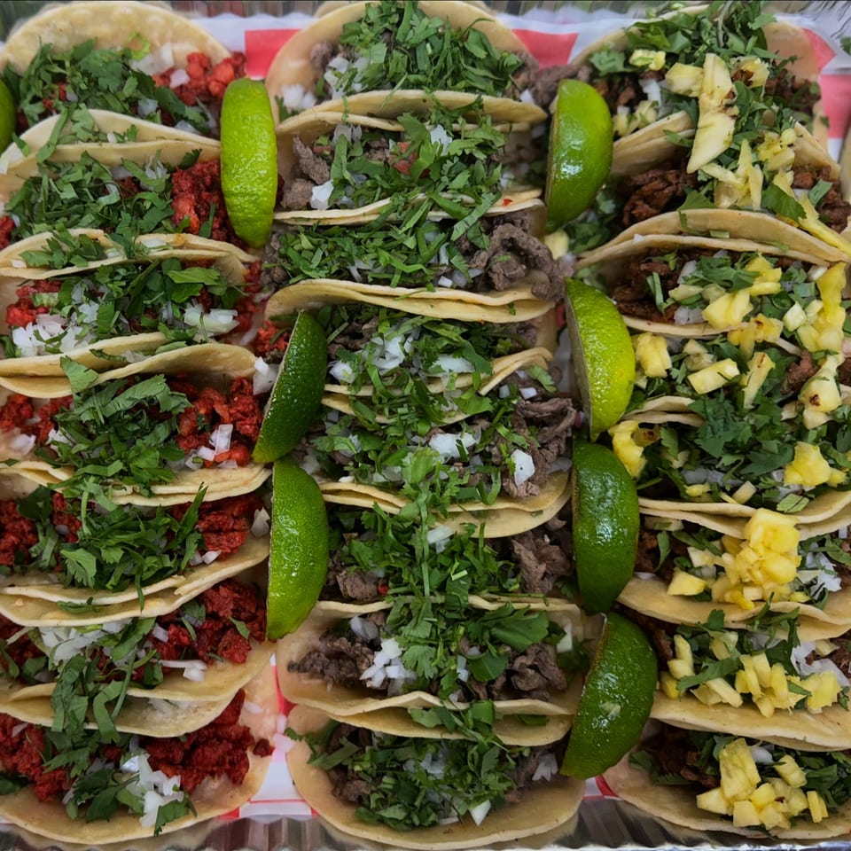 A tray of Tacos la Gringa's Mexican tacos, with various fillings, cilantro, onions, and lime wedges.
