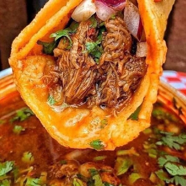 A birria taco from Tacos la Gringa, filled with shredded meat, cilantro, and onions, dipped in consommé.