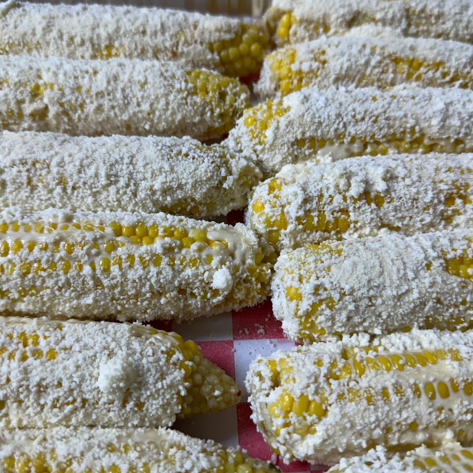 Close-up of several elotes, Mexican street corn, coated in white cheese and mayonnaise.