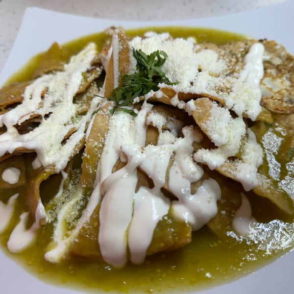 Chilaquiles with green salsa, sour cream, crumbled cheese, and cilantro on a white plate.