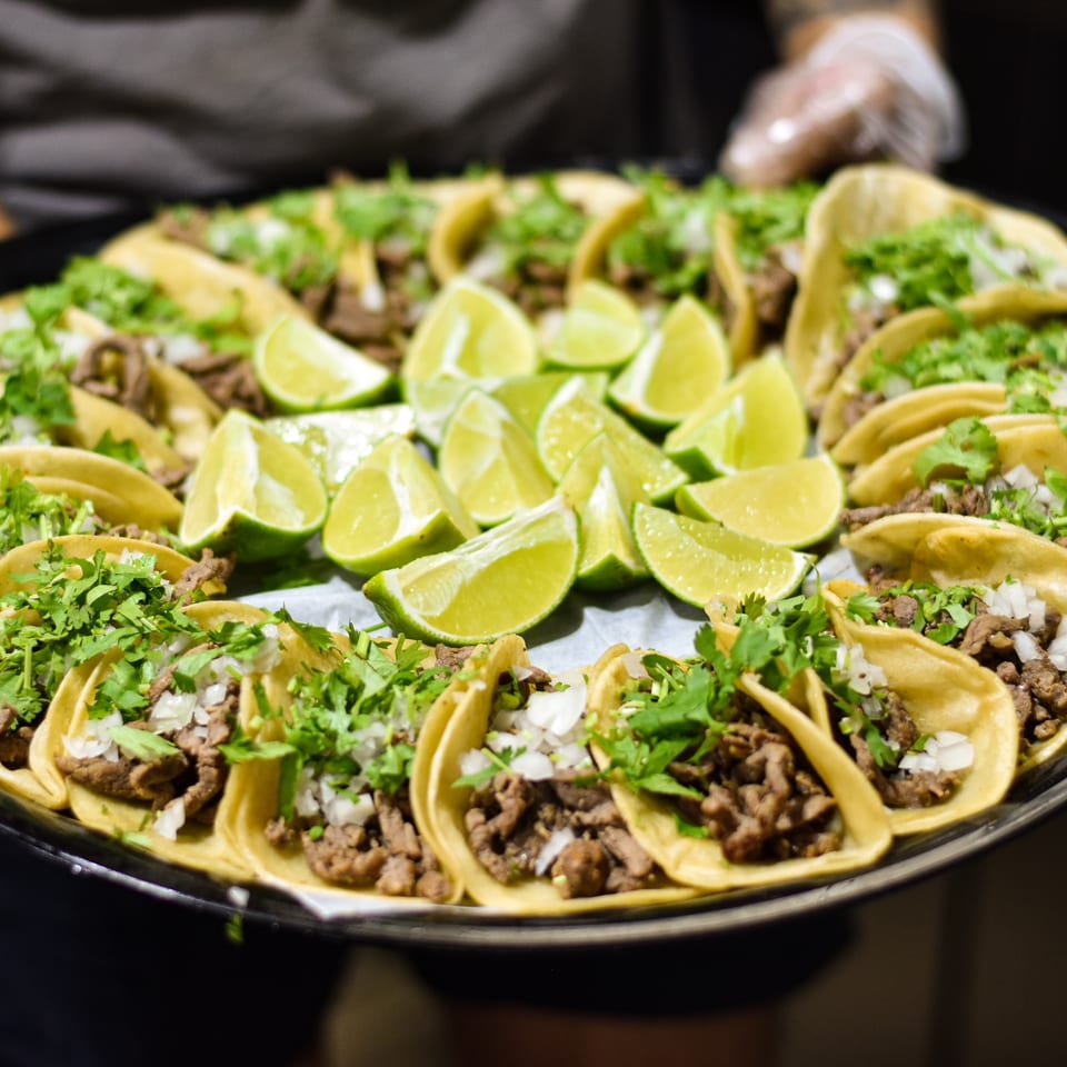 A tray of Tacos la Gringa's Mexican tacos with meat, cilantro, onions, and lime wedges.