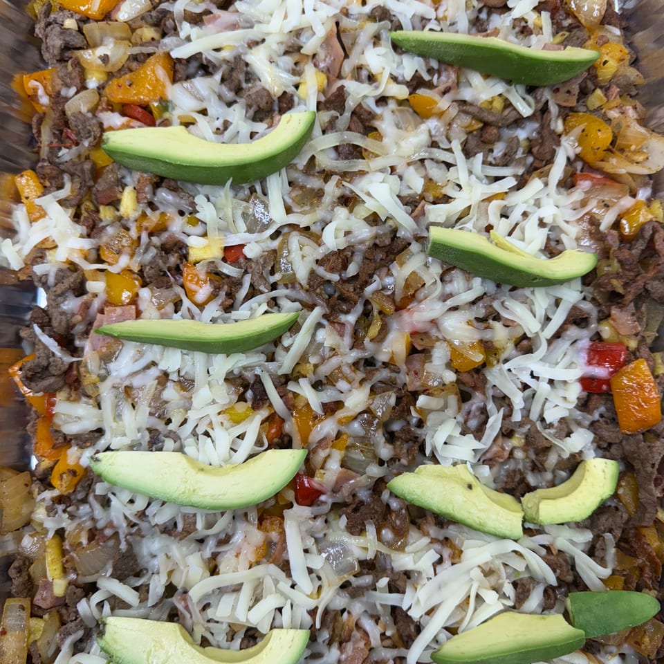 Close-up of Tacos la Gringa's Mexican dish with meat, peppers, onions, melted cheese, and avocado slices.