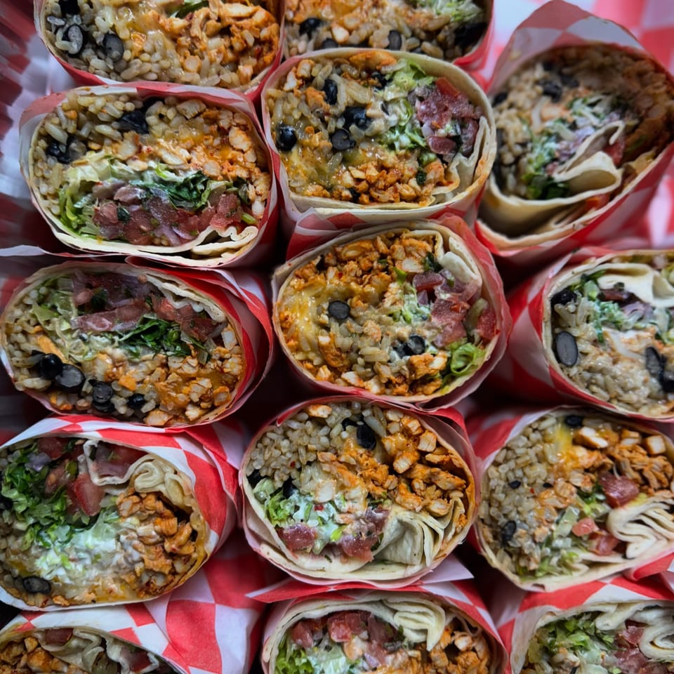 Overhead view of multiple Tacos la Gringa burritos, cut in half, revealing fillings of chicken, rice, beans, and vegetables.